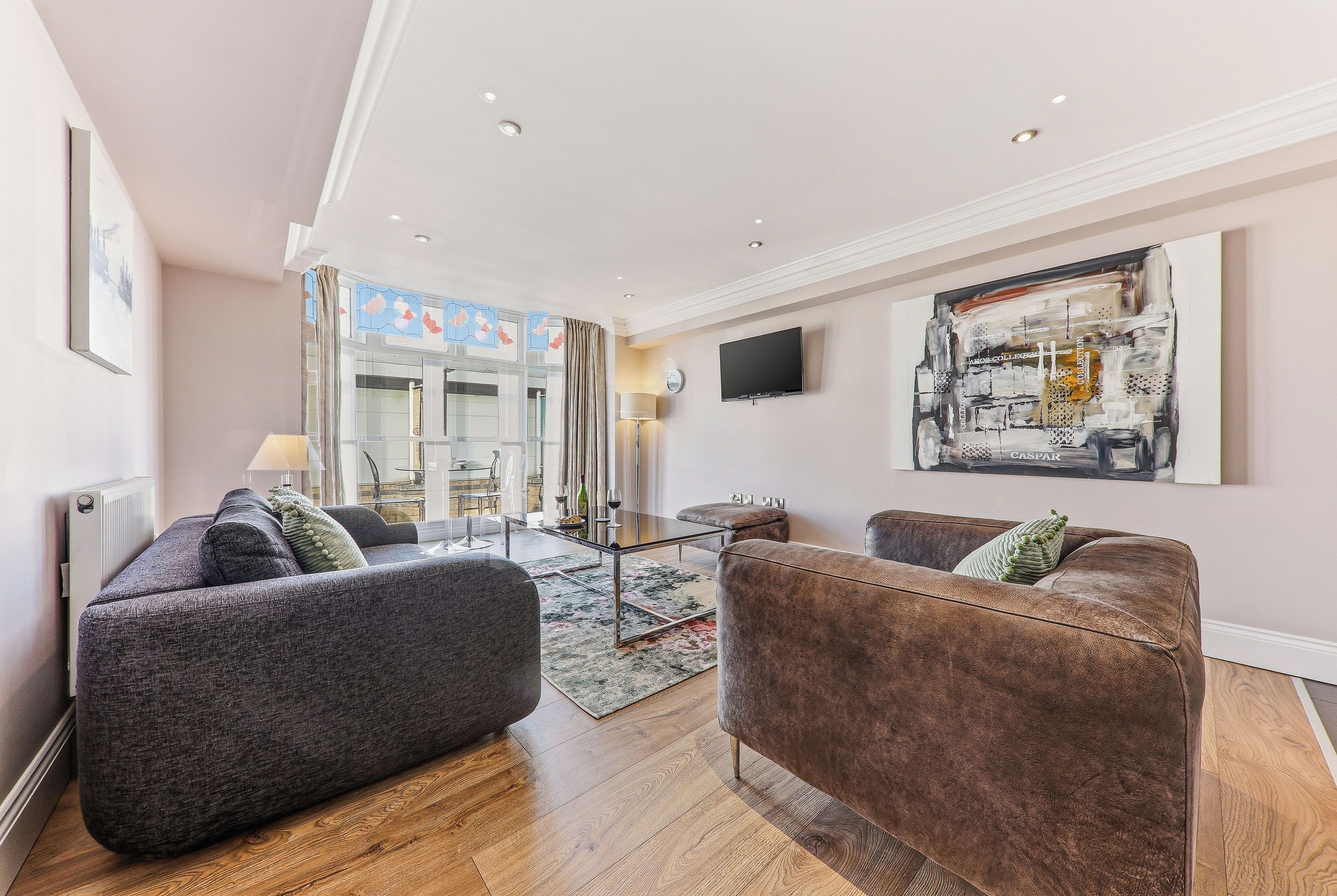 A modern living room with two sofas, a flat-screen TV, and a large abstract painting.
