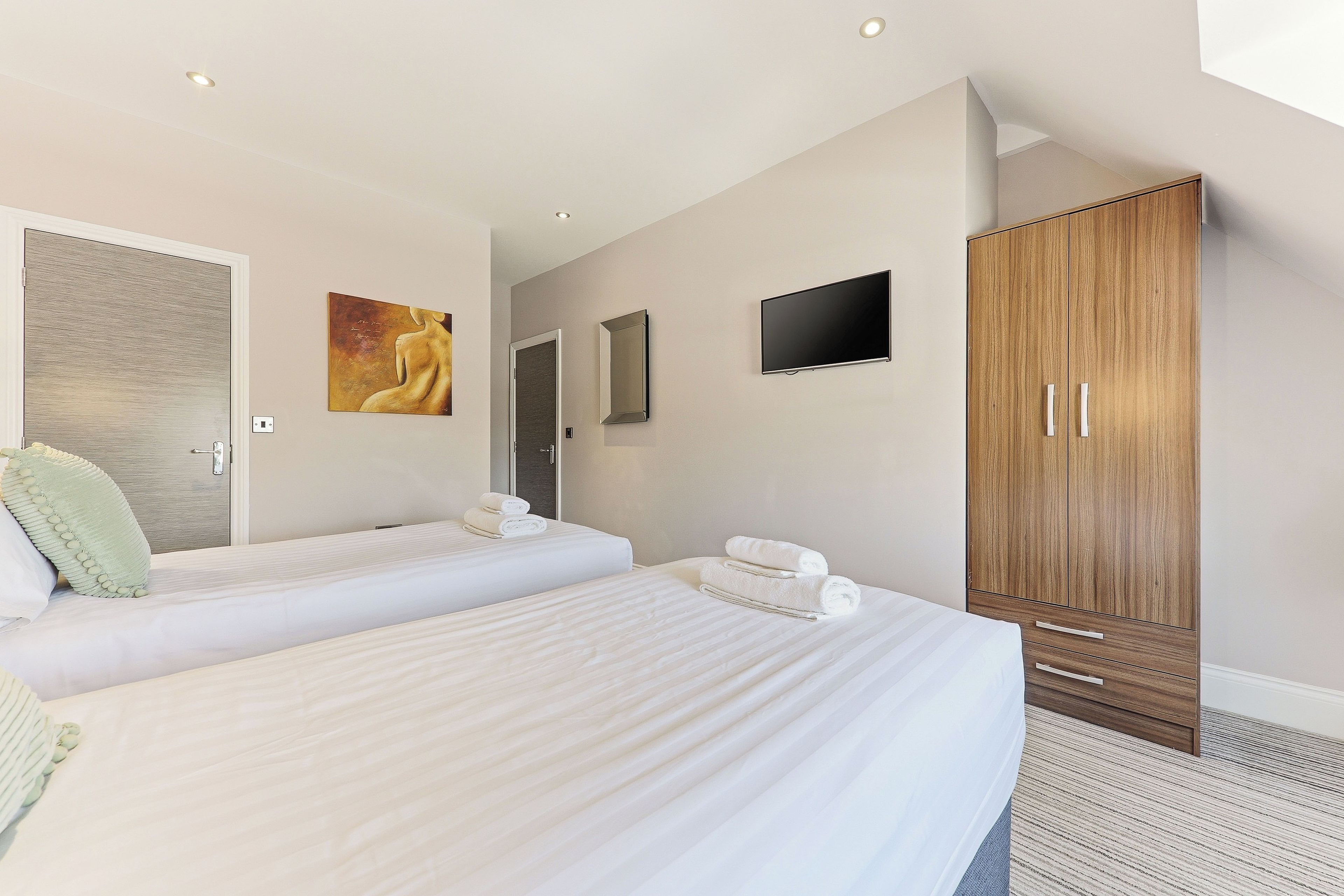 A hotel room with two beds, a wardrobe, a flat-screen TV, and artwork on the walls.