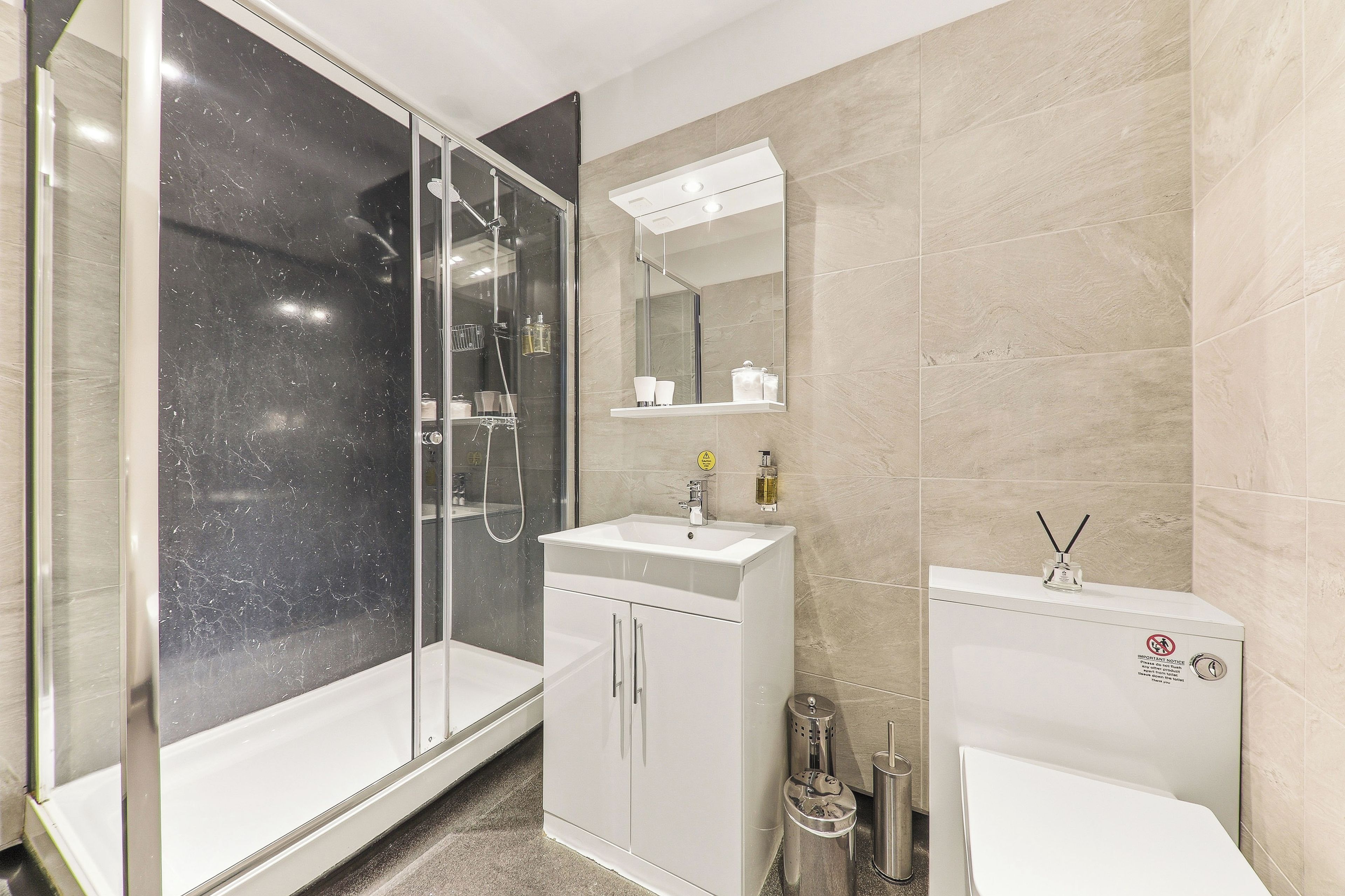Een moderne badkamer met een douchecabine van glas, een witte wastafel en een toilet.