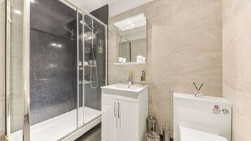 Een moderne badkamer met een douchecabine van glas, een witte wastafel en een toilet.