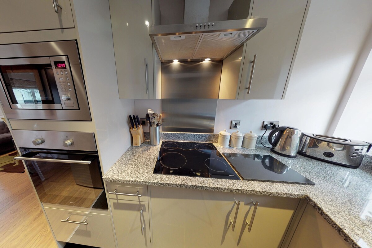 Una cocina moderna con electrodomésticos de acero inoxidable, encimeras de granito y microondas integrado.