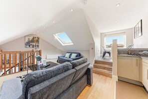 A spacious loft with a high ceiling, a skylight, a staircase, a living area with a sofa, and a kitchen area.
