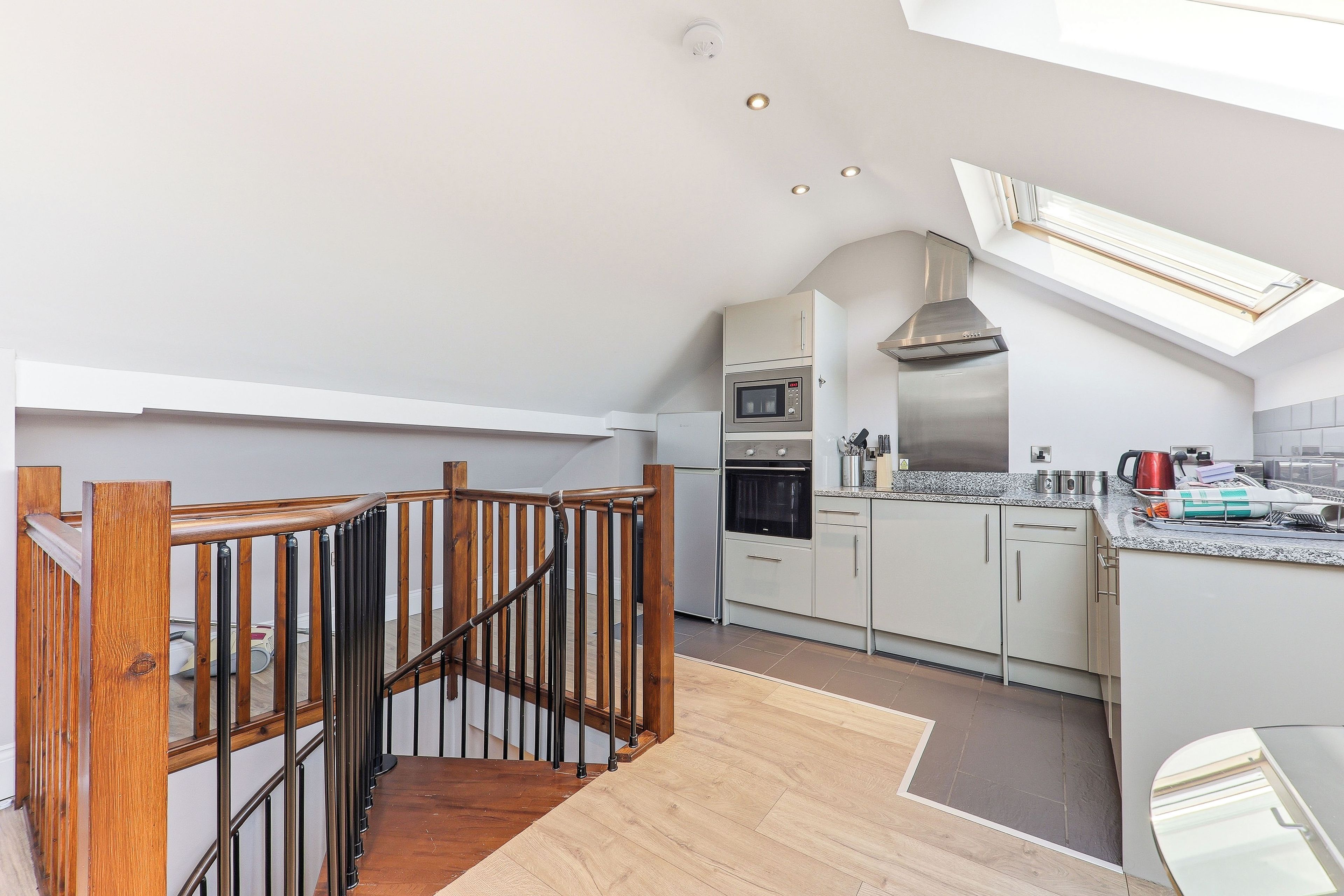 A modern kitchen with a skylight, built-in appliances, and a wooden staircase.
