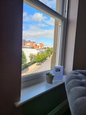 Una ventana con vista a una calle, una planta en maceta y un papel en el alféizar.