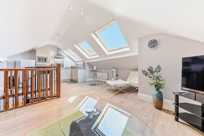 Un loft espacioso con cocina, comedor y sala de estar con televisor y planta.