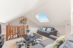 Ein geräumiges Loft mit hoher Decke, einem Oberlicht, einer Treppe, einer Couch, einem Couchtisch und einem gemusterten Teppich.