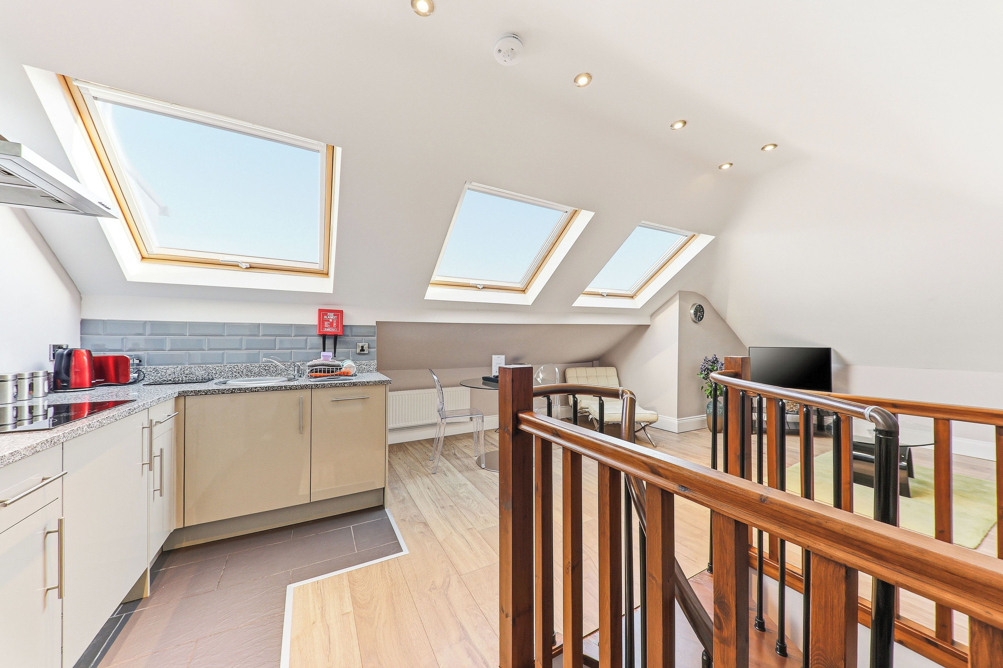 A modern kitchen with skylights, a dining area with a table and chairs, and a wooden staircase.