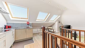 A modern kitchen with skylights, a dining area with a table and chairs, and a wooden staircase.