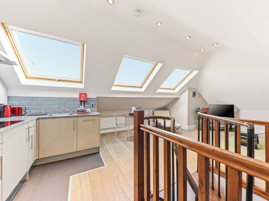 A modern kitchen with skylights, a dining area with a table and chairs, and a wooden staircase.