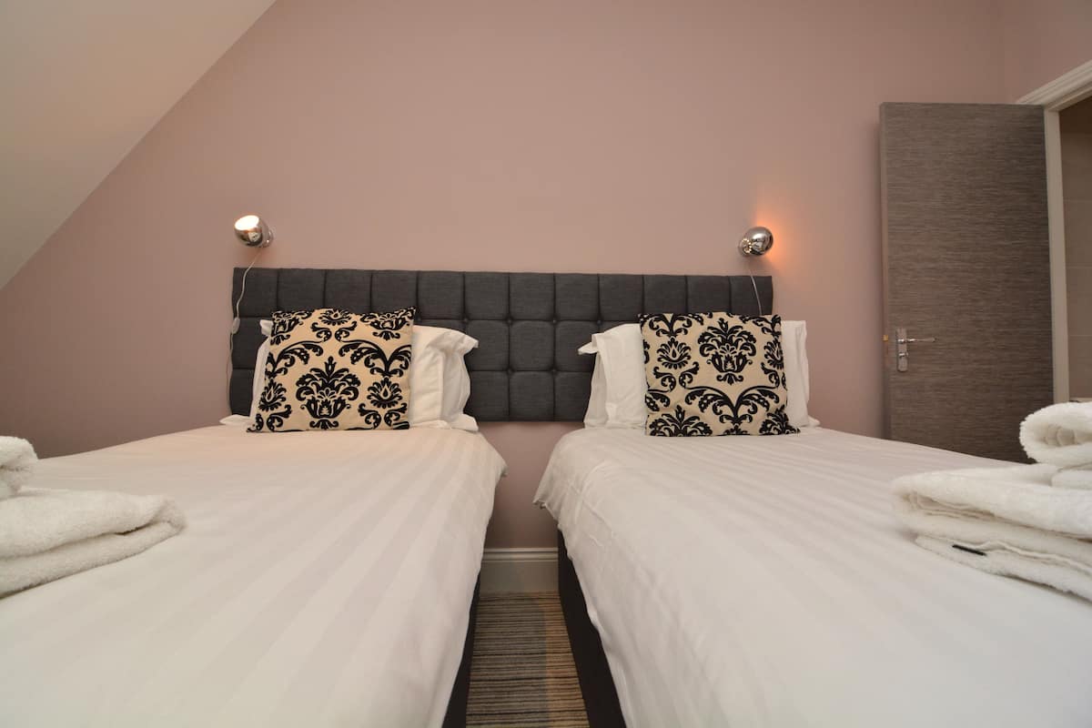 A hotel room with two beds, a dark headboard, and a door to the right.