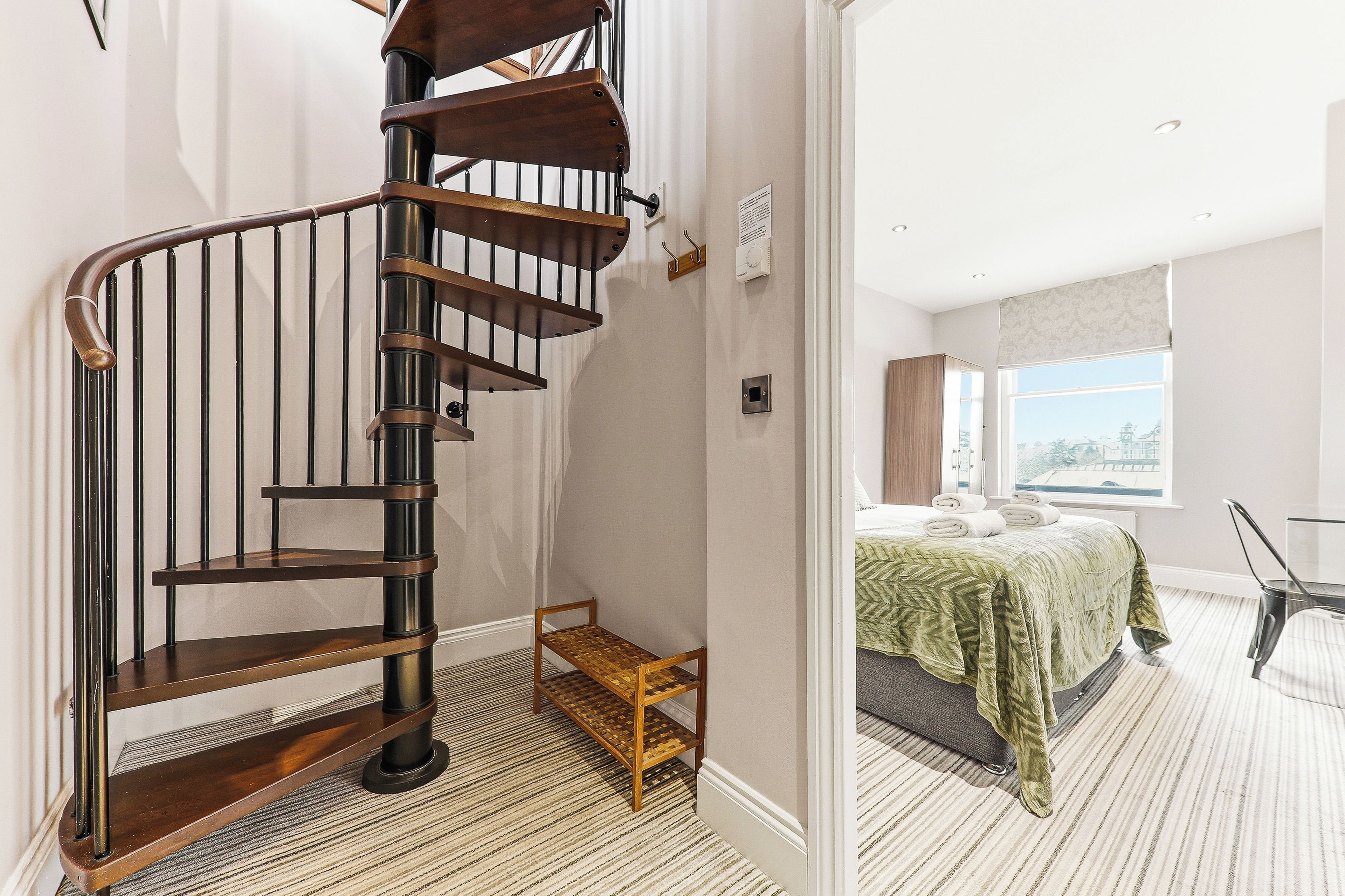 Een spiraaltrap met houten treden en metalen leuningen die leidt naar een slaapkamer met een bed en uitzicht op de stad.
