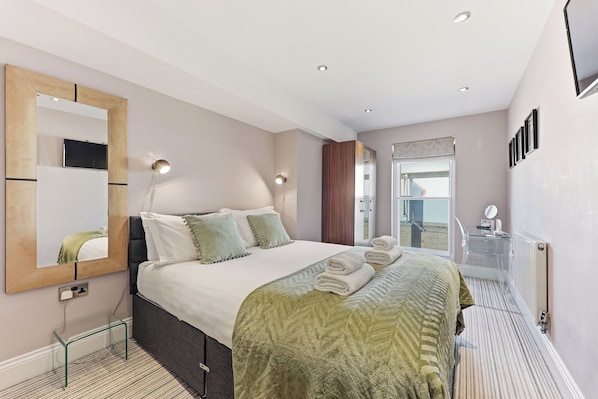 Habitación de hotel con cama, espejo, mesita de noche, radiador y ventana.