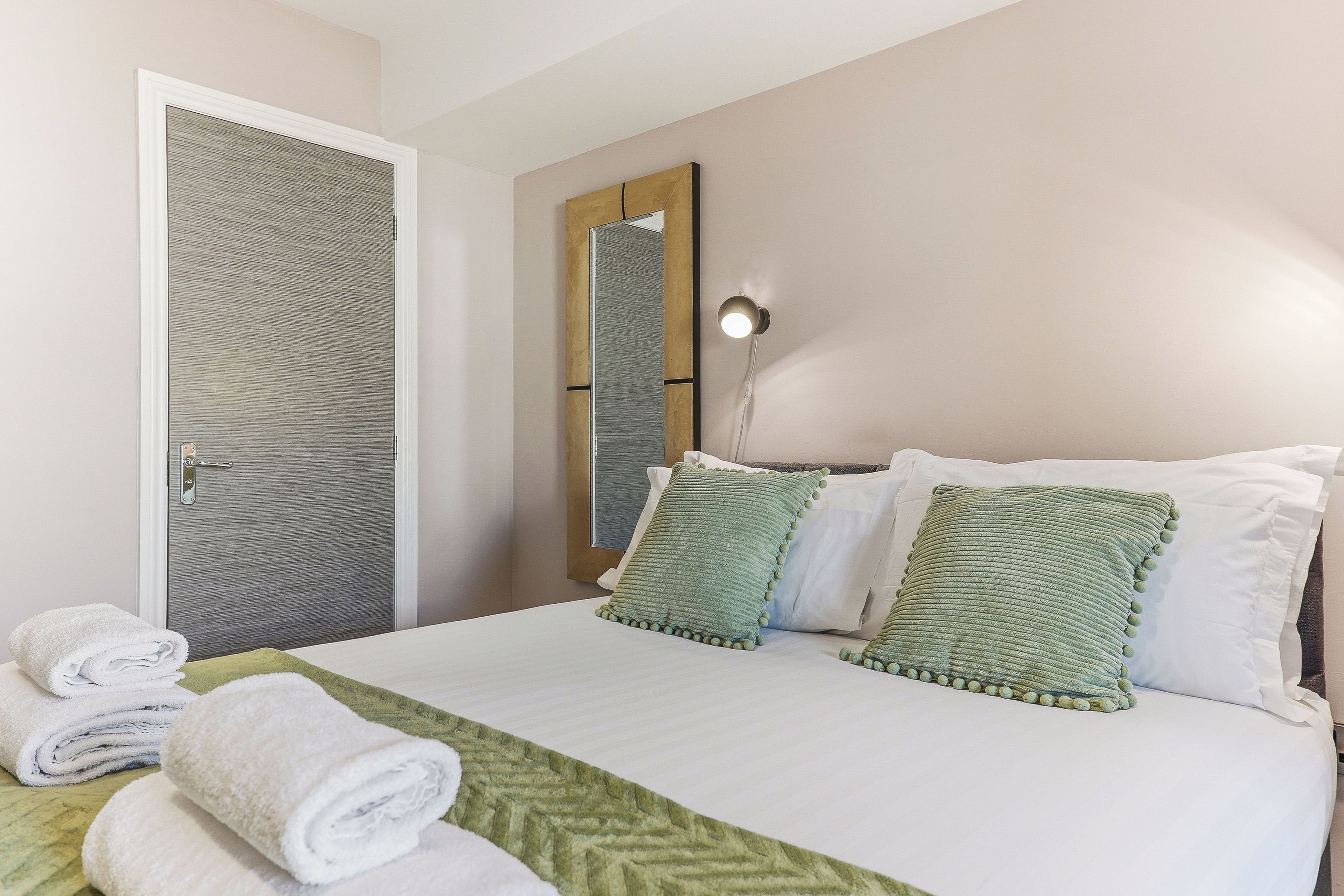Ein Hotelzimmer mit Bett, Spiegel, Wandlampe und Tür.