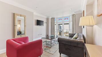 A modern living room with a red armchair, a grey sofa, a flat-screen TV, and a large window with curtains.