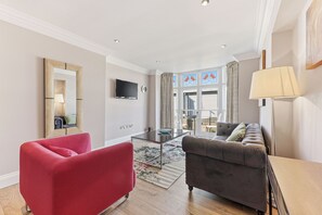 Una sala de estar moderna con un sillón rojo, un sofá gris, un televisor de pantalla plana y un ventanal con cortinas.