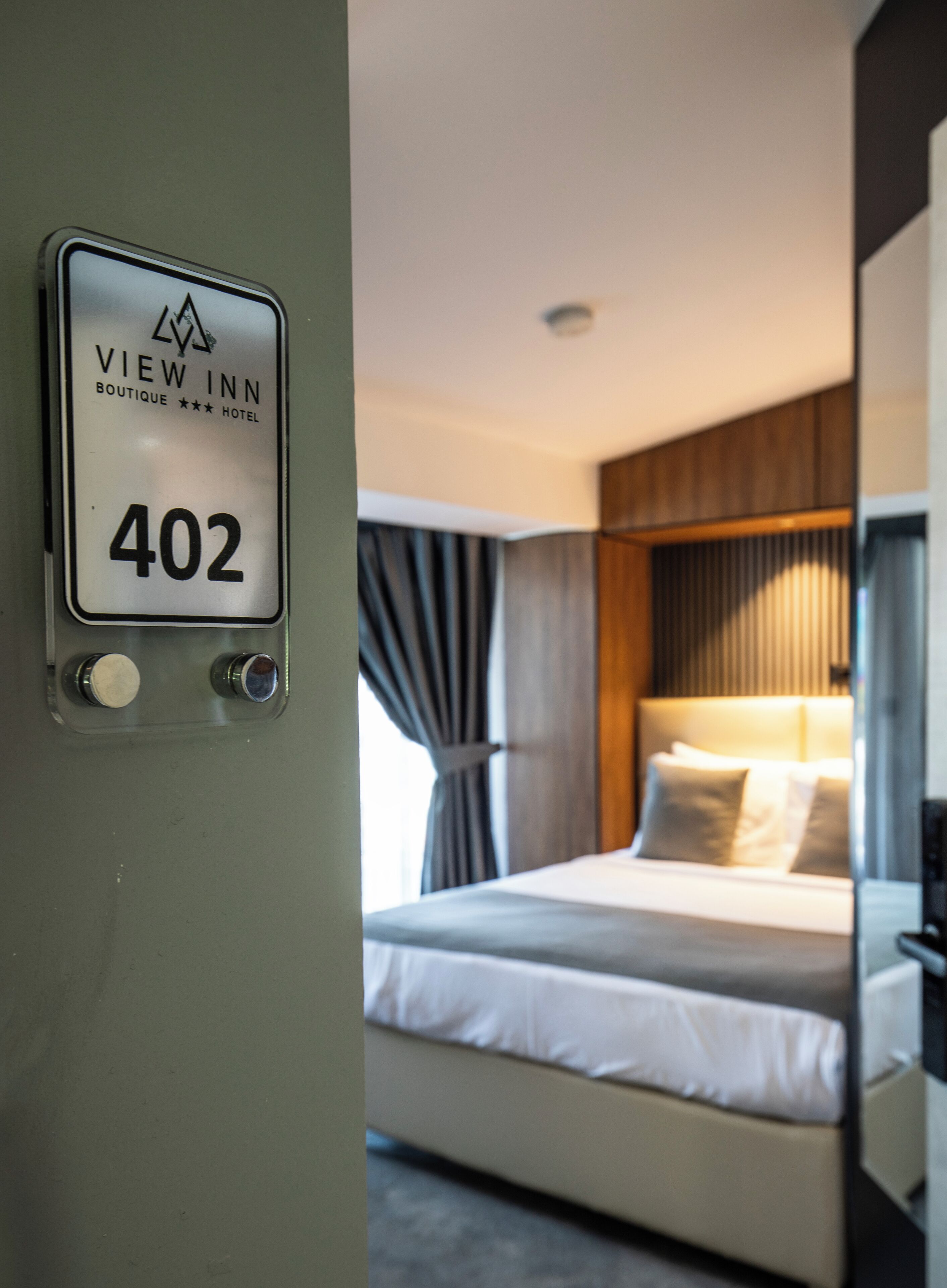 Een hotelkamer met een bed, een groot raam en een bordje met daarop kamer 402.