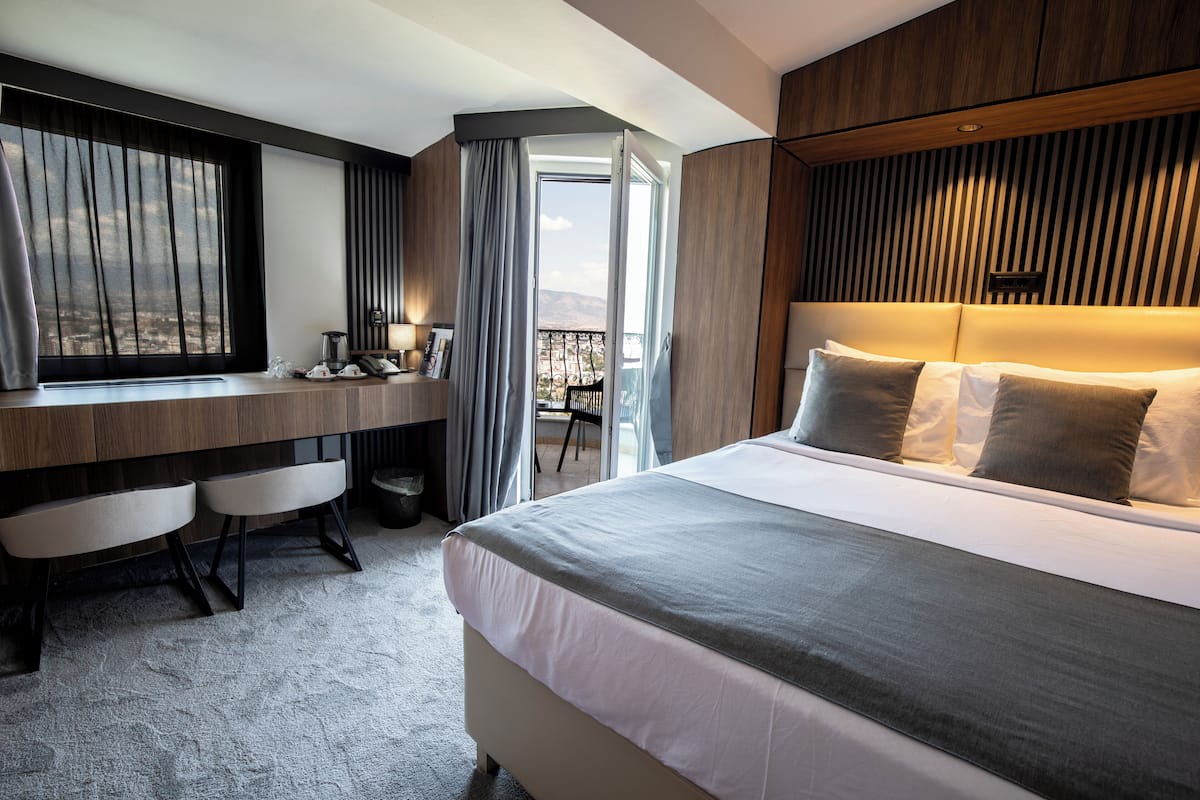 A hotel room with a large bed, a desk with chairs, and a view of the outdoors.