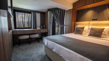 A modern hotel room with a large bed, a desk with chairs, and a view of the outdoors through the window.