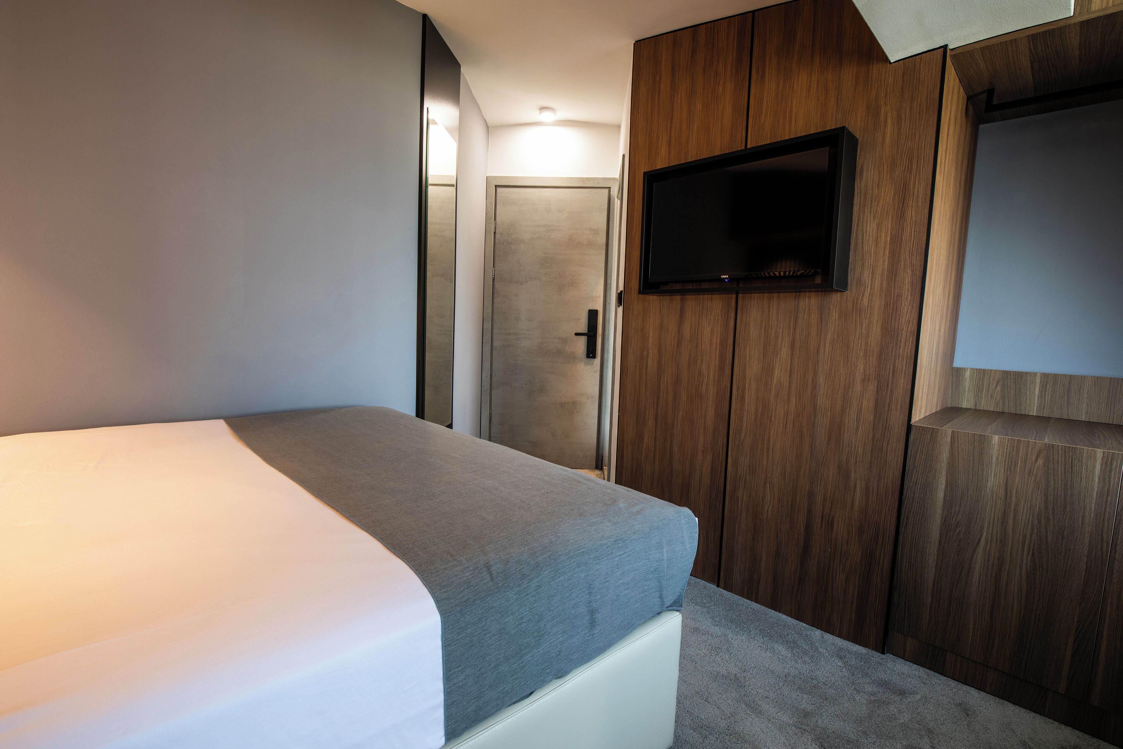 Un dormitorio moderno con una cama, televisión montada en la pared y una puerta que da a otra habitación.