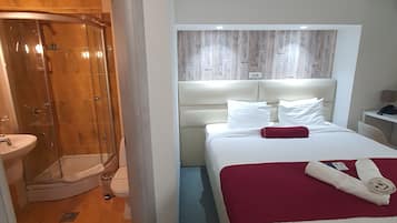 Ein Hotelzimmer mit Dusche, einem Bett mit roter Decke und einem Kopfteil mit Holzpaneelen.
