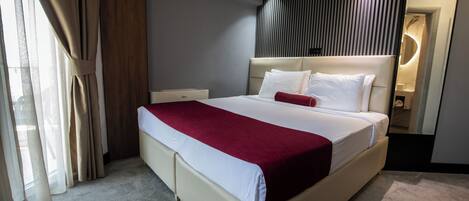 Quarto de hotel moderno com uma cama grande, mesa de cabeceira, espelho e vista para o exterior.
