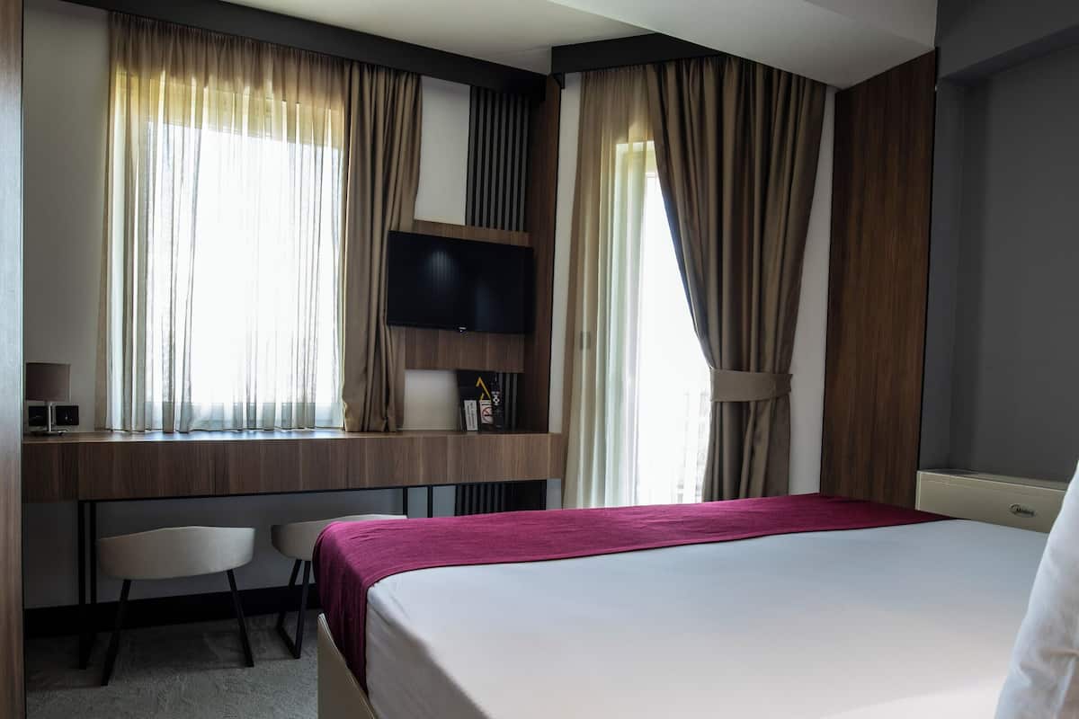 A hotel room with a large bed, a desk with a chair, a television, and curtains.