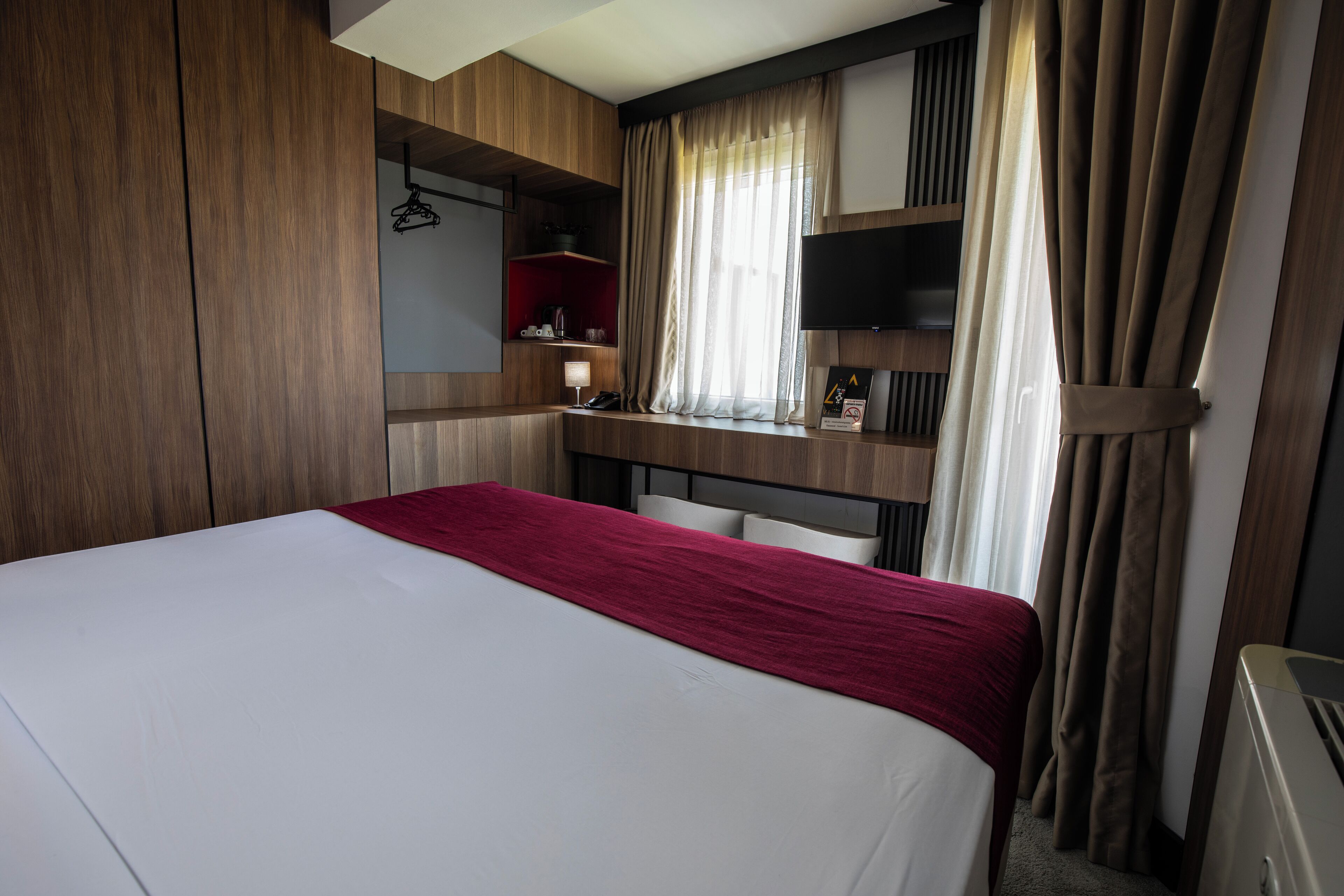 Una habitación de hotel con cama, escritorio, silla, televisión y ventana con cortinas.