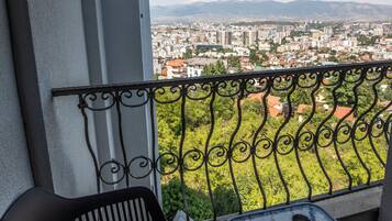 A balcony with a view of a cityscape, a black metal chair, and a small table with a cup.
