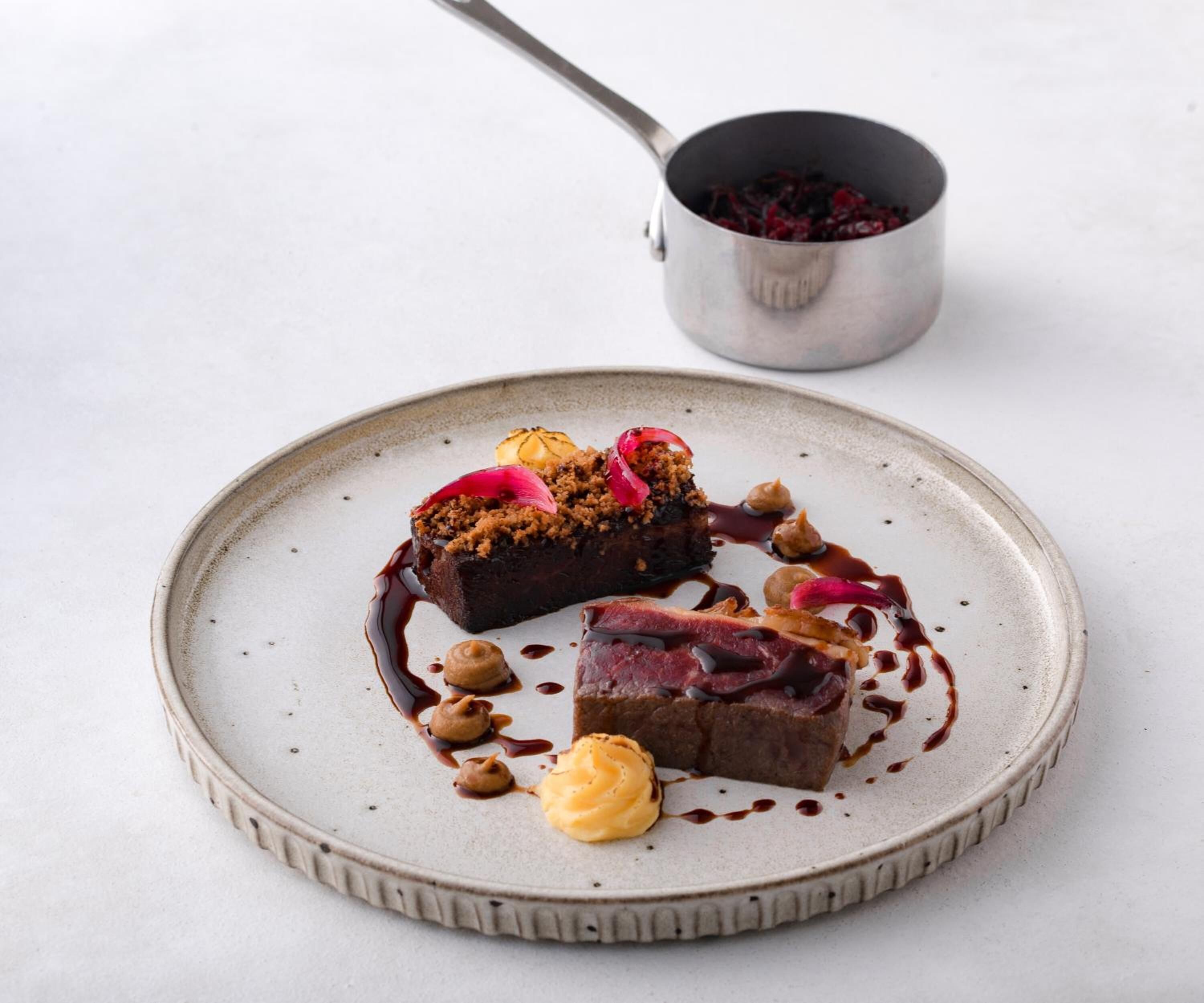 A dessert plate with a slice of cake, sauce, and garnishes on a ceramic plate.