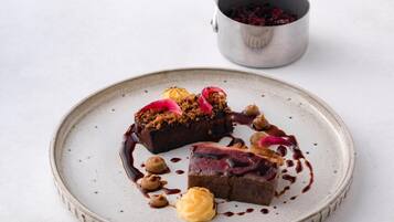 A dessert plate with a slice of cake, sauce, and garnishes on a ceramic plate.