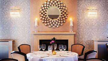 A dining area with a round table set for six, a decorative mirror above, and a fireplace with candles.