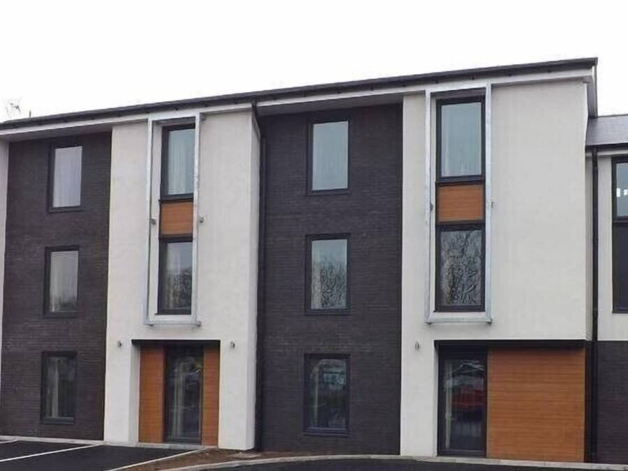 A multi-story residential building with a modern design, featuring a combination of white and dark-colored facades, large windows, and wooden door frames.