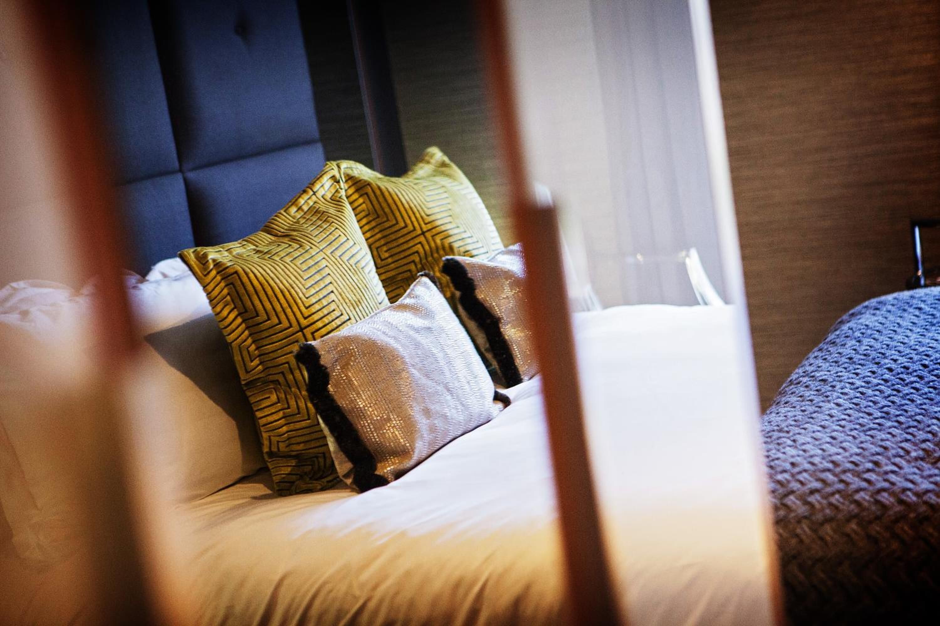 A neatly made bed with multiple pillows, a dark headboard, and a window with curtains.