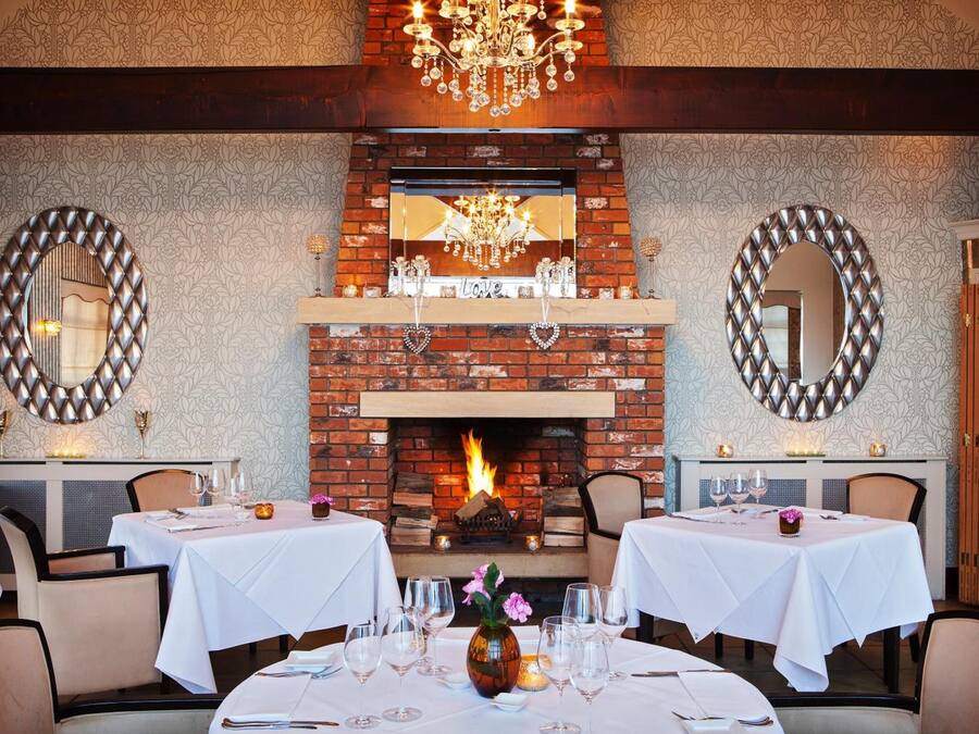 Un restaurante con chimenea de ladrillo, manteles blancos y candelabros.