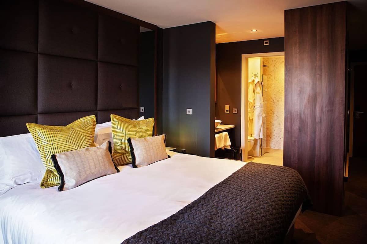 Een moderne hotelkamer met een groot bed, een donker hoofdeinde en een badkamer door een open deur zichtbaar.