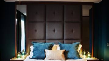 Una cama bien hecha con almohadas azules y beige, un cabecero capitonado y lámparas de noche.