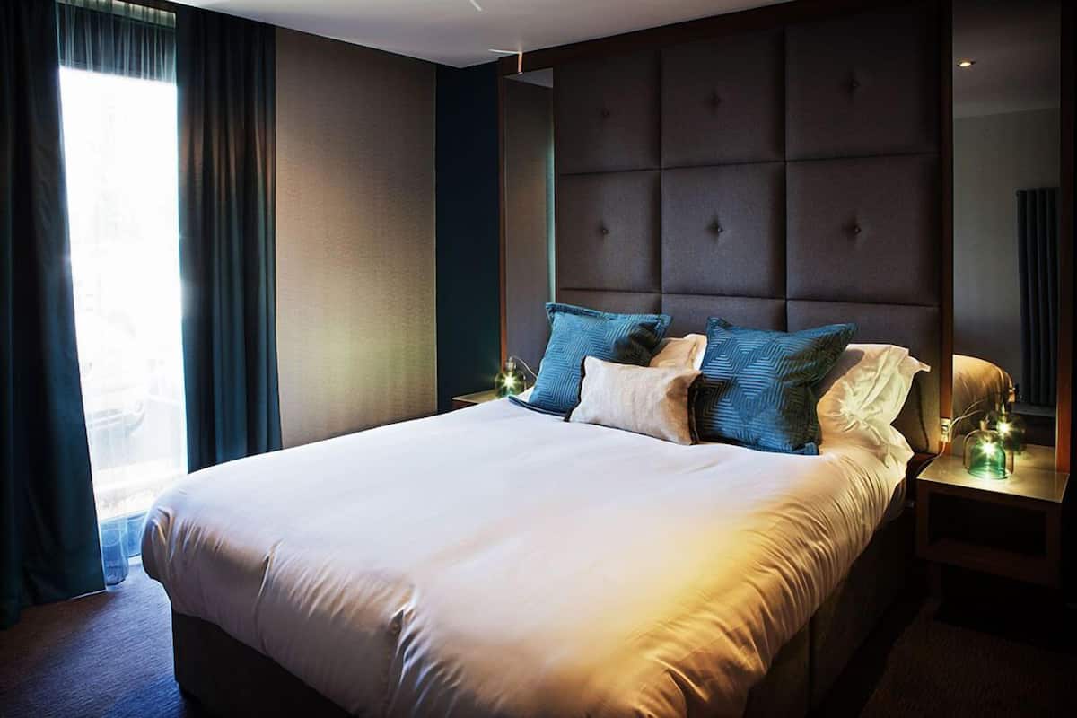Een groot bed met veel kussens, een hoofdbord en een nachtkastje met een lamp.