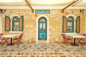 A stone-walled room with a tiled floor, two windows with shutters, and a table with chairs. - Can Mocamp (Kas)