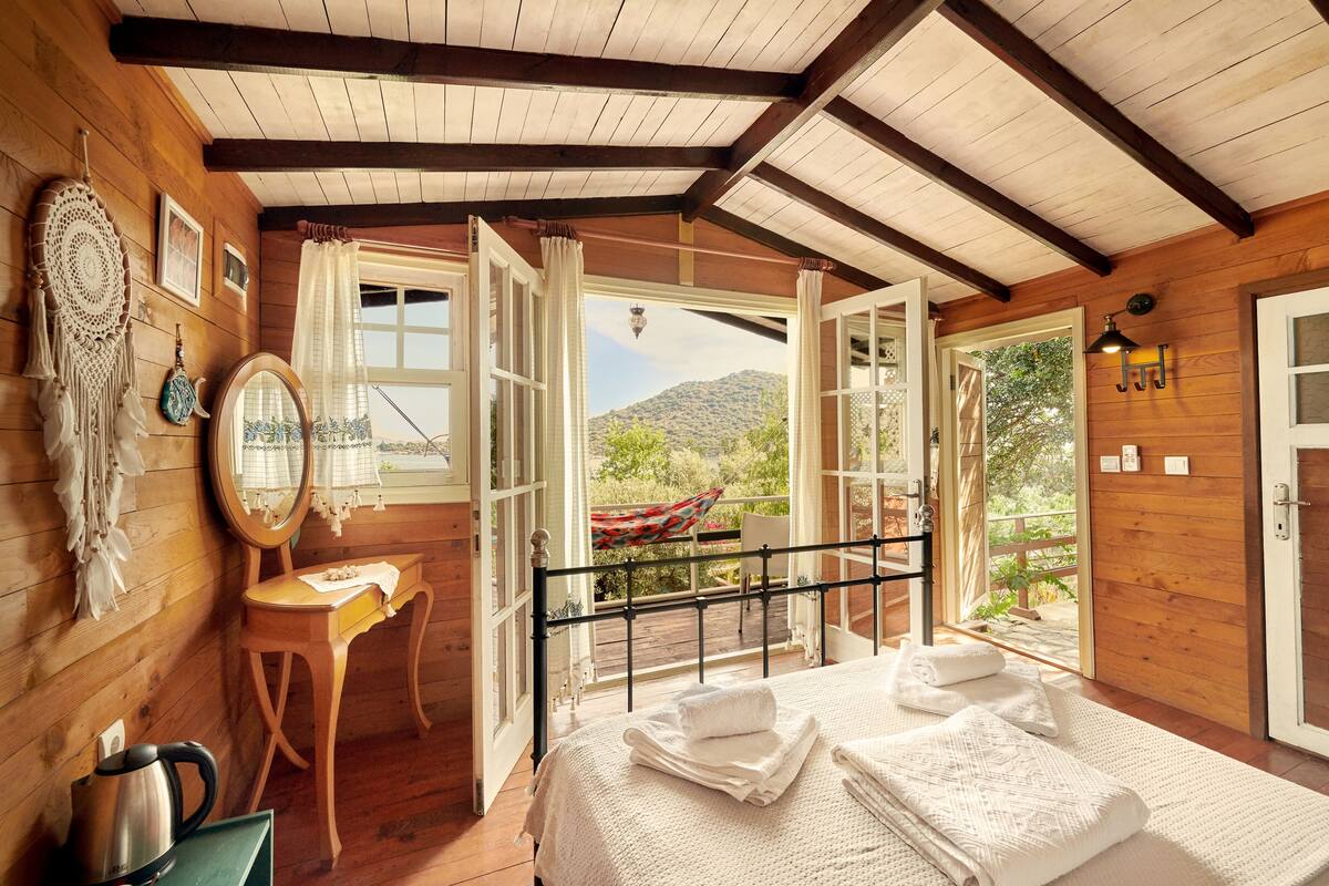 A wooden cabin room with a bed, a desk, and a view of the outdoors.