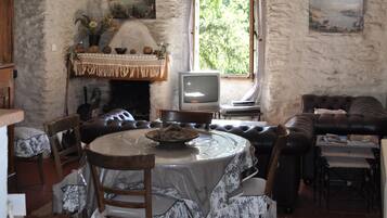 A rustic dining area with a stone wall, a fireplace, a television, and a cozy seating arrangement.