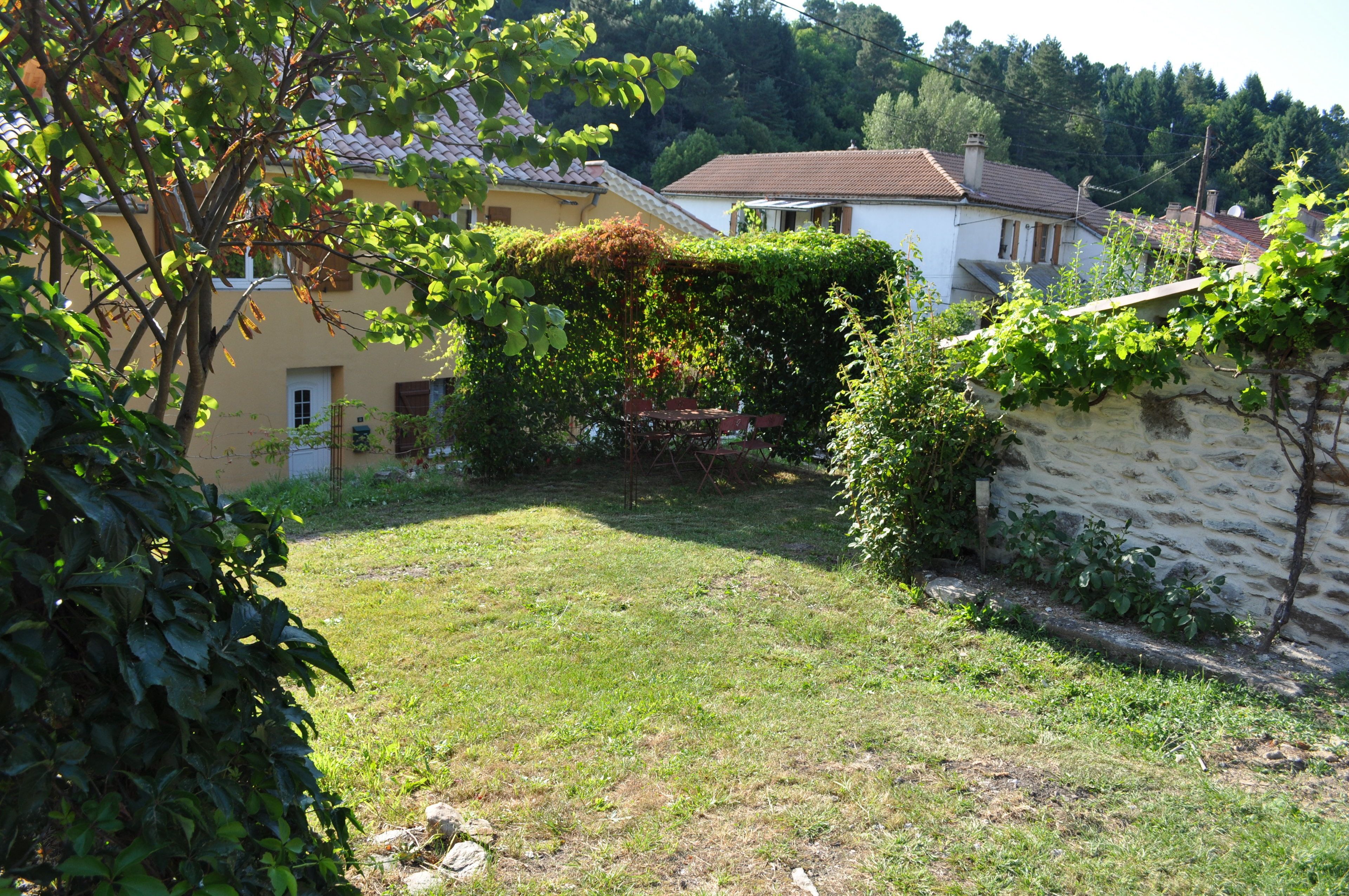 A garden with a grassy lawn, a stone wall, and a building with a tiled roof.