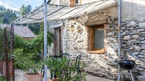 A rustic stone building with a covered patio, outdoor seating, and a barbecue grill. - La Ribeyrette (Chamborigaud)
