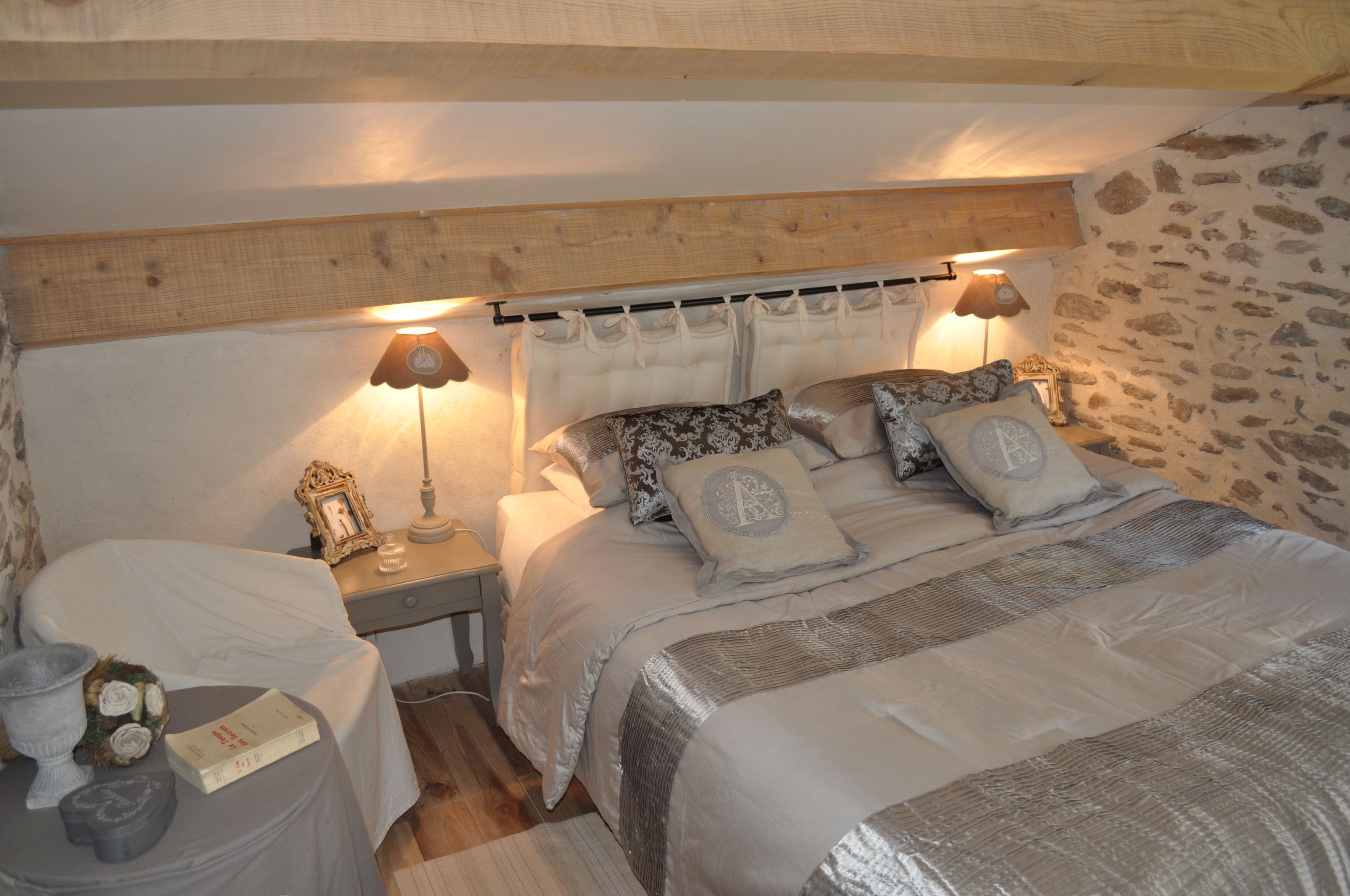 A cozy bedroom with a bed, bedside tables, lamps, and a stone wall.