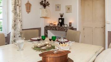 A dining table set with plates, glasses, and candles, with a copper pot and a basket of bread on the table.