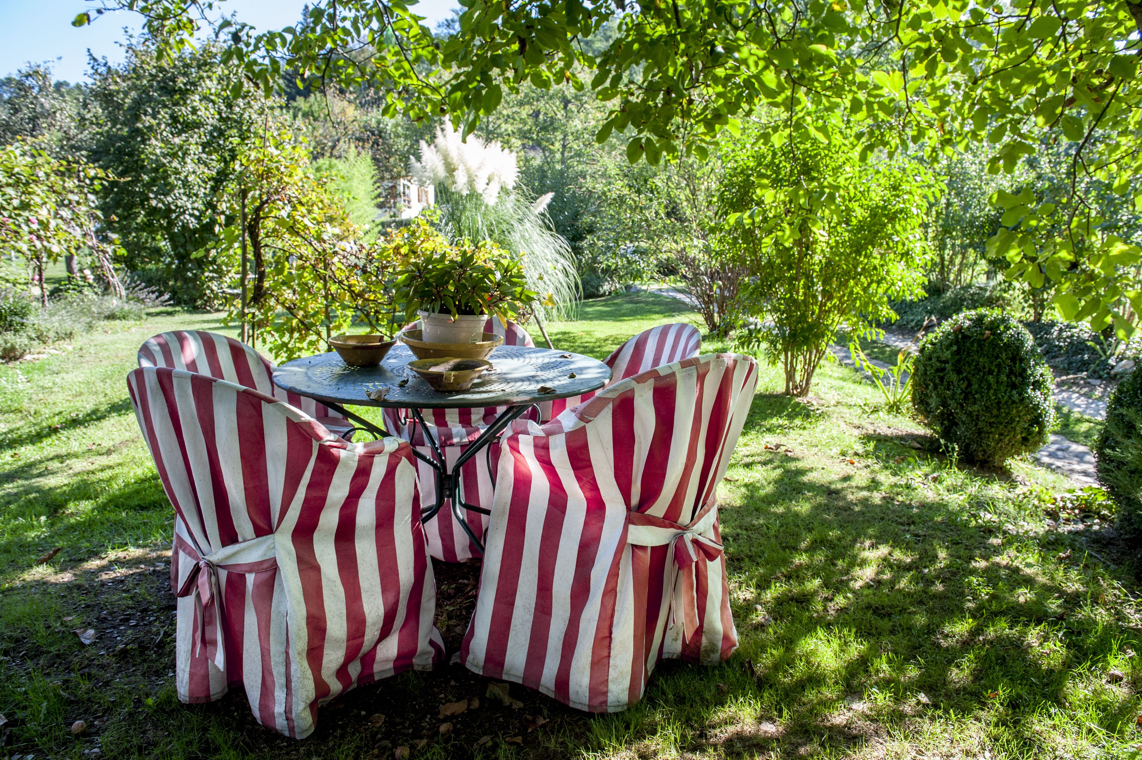 Une table ronde entourée de chaises à rayures, le tout installé dans un jardin.