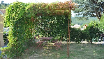 Um jardim com pérgola coberta por trepadeiras, uma mesa e cadeiras.