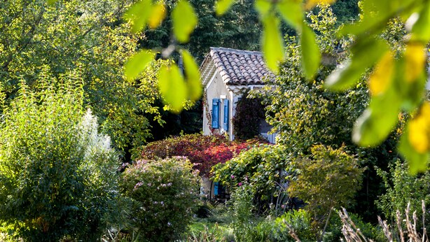 A small house with a tiled roof surrounded by lush greenery and flowering plants. - La Ribeyrette (Chamborigaud)