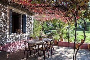 Ein Essbereich im Freien mit Tisch und Stühlen, umgeben von Kübelpflanzen und Blick auf einen Garten.