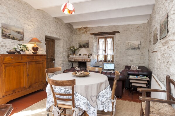 Una habitación rústica con pared de piedra, muebles de madera, chimenea y una mesa de comedor con sillas.