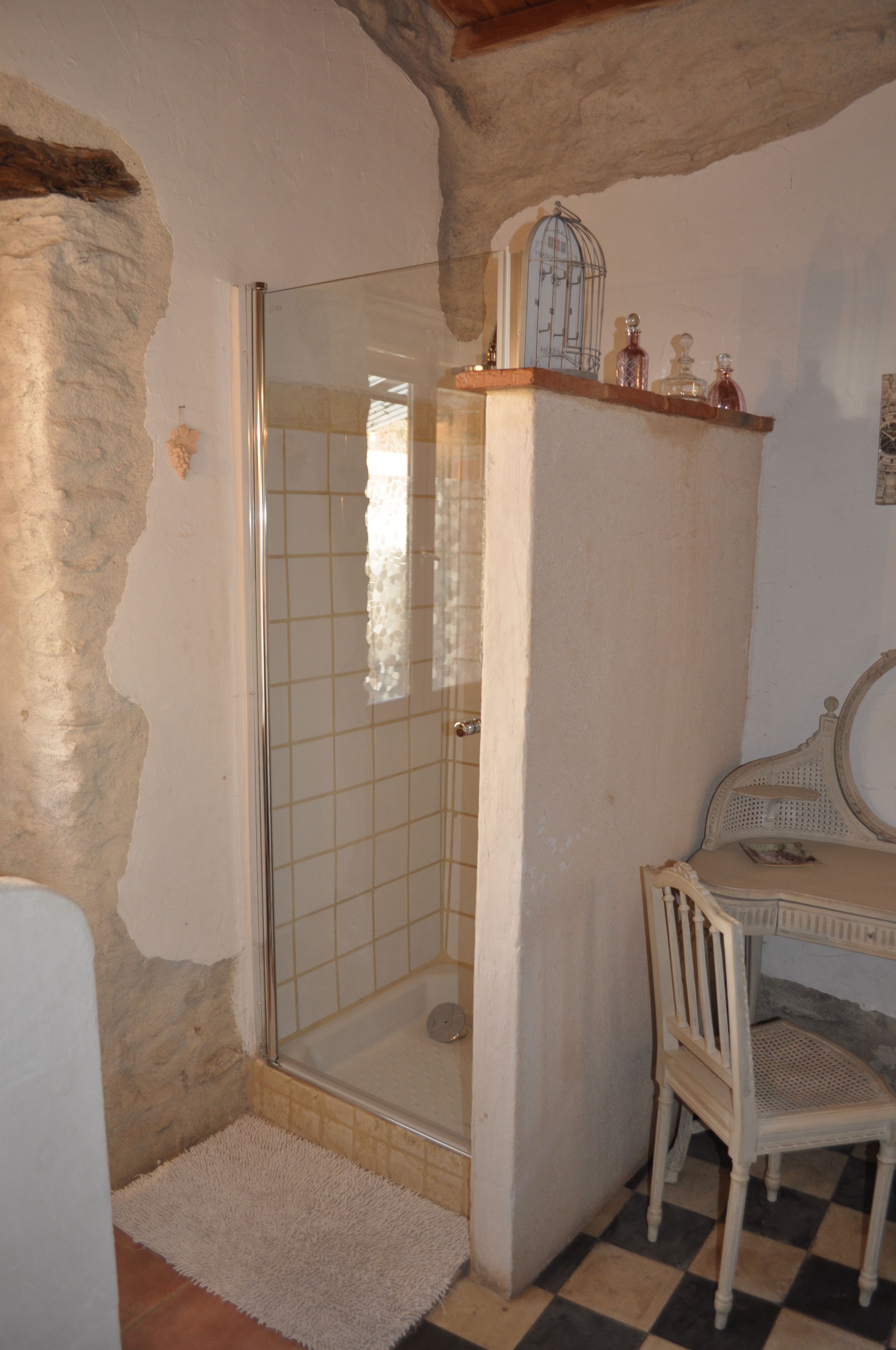 A bathroom with a glass shower, a white chair, and a shelf with bottles.